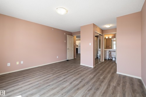 Expansive room featuring wood-finish flooring, a neutral wall color, and a full bathroom with a vanity and mirror - 406 16035 132 Street, Edmonton, AB - Indoor Photo Showing Other Room