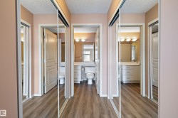 Hallway featuring wood-finish flooring, mirrored sliding closet doors, and light-toned walls - 