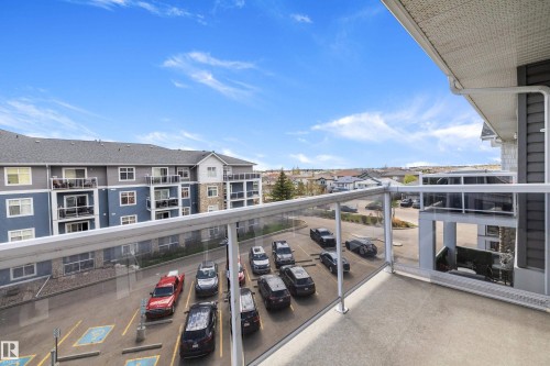 Private balcony with concrete flooring and clear glass railing, offering an elevated perspective of the surrounding structures and paved parking area - 406 16035 132 Street, Edmonton, AB - Outdoor With Balcony With Exterior