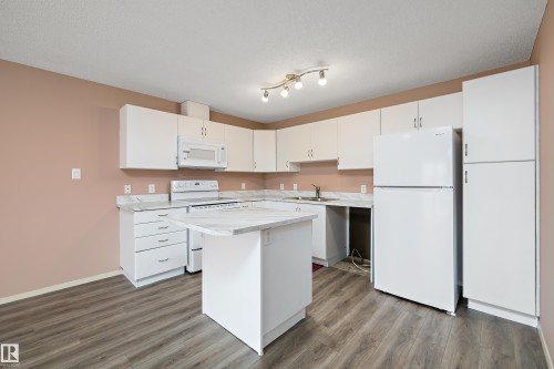 Modern kitchen featuring white cabinetry, a built-in island, laminate wood-finish flooring, a white range, and a white refrigerator - 406 16035 132 Street, Edmonton, AB - Indoor Photo Showing Kitchen