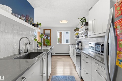 Sleek kitchen featuring white flat-panel cabinetry, light gray countertops, and an elongated hexagonal tile backsplash - 217 14819 51 Avenue, Edmonton, AB - Indoor Photo Showing Kitchen With Upgraded Kitchen