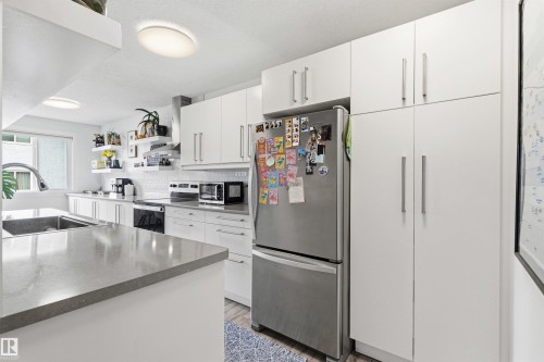 Modern kitchen featuring white cabinetry, integrated stainless steel appliances, a large single-basin sink, and a contrasting countertop - 217 14819 51 Avenue, Edmonton, AB - Indoor Photo Showing Kitchen