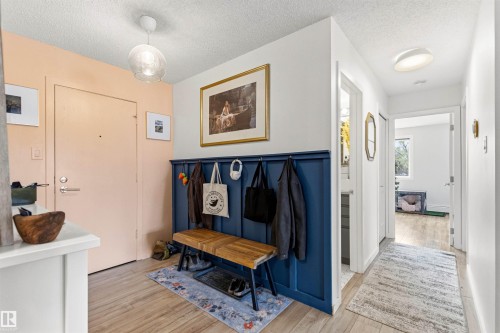 Entryway featuring wood-finish flooring, a built-in coat rack with a wooden bench, and a modern pendant light fixture - 217 14819 51 Avenue, Edmonton, AB - Indoor Photo Showing Other Room