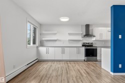 Modern kitchen featuring light wood-finish flooring, white cabinetry with silver hardware, a stainless steel range with overhead hood, a window, and open shelving - 