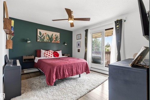 Room featuring wood-finish flooring, a full-light sliding door with access to an outdoor space, a ceiling fan with integrated lighting, and a painted accent wall - 217 14819 51 Avenue, Edmonton, AB - Indoor Photo Showing Bedroom