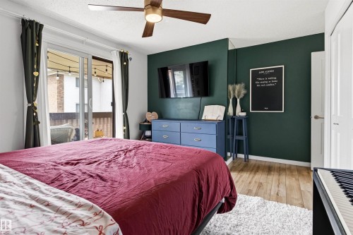 Spacious bedroom featuring wood-finish flooring, a contemporary ceiling fan, and sliding glass doors opening to an outdoor area - 217 14819 51 Avenue, Edmonton, AB - Indoor Photo Showing Bedroom