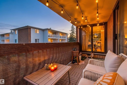 Private balcony featuring string lighting, sliding glass doors, a slatted privacy screen, and composite deck tiles - 217 14819 51 Avenue, Edmonton, AB - Outdoor With Balcony With Exterior