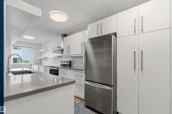 Modern kitchen featuring extensive white cabinetry, a stainless steel refrigerator, and a kitchen island with an undermount sink - 