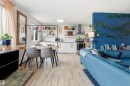 Open-concept living area featuring wood-finish flooring, a kitchen with white cabinetry, stainless steel appliances, and a range hood, and a dining area with a modern light-toned table - 217 14819 51 Avenue, Edmonton, AB  - Indoor 