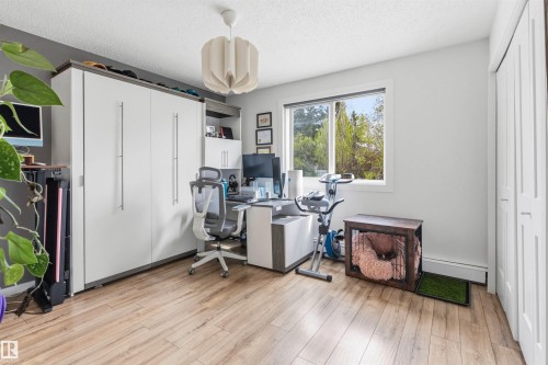 Wood-finish flooring throughout, featuring a built-in wall storage unit with white panel doors and silver handles - 217 14819 51 Avenue, Edmonton, AB - Indoor Photo Showing Office