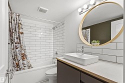 Full bathroom featuring a rectangular vessel sink with chrome faucet, a large round mirror, and a built-in bathtub with subway tile surround - 