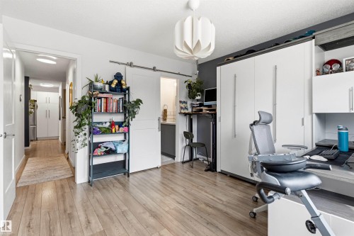 Spacious room featuring wood-finish flooring and a white barn door - 217 14819 51 Avenue, Edmonton, AB - Indoor