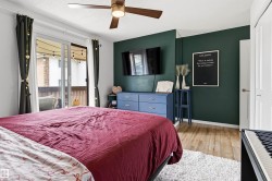 Spacious bedroom featuring wood-finish flooring, a contemporary ceiling fan, and sliding glass doors opening to an outdoor area - 