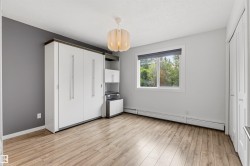 Room featuring wood-finish flooring, a built-in white cabinetry system with integrated shelving, and a prominent window with roller blinds - 