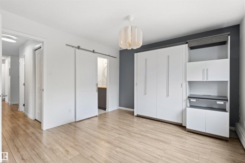 Wood-finish flooring throughout, complemented by a white ceiling and a contemporary pendant light fixture - 217 14819 51 Avenue, Edmonton, AB 
