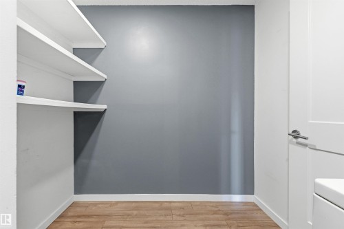 Built-in shelving with white finishes, wood-finish flooring, and a modern interior door with brushed nickel hardware - 217 14819 51 Avenue, Edmonton, AB 