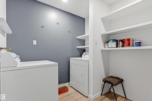 Dedicated laundry area featuring a light wood-finish floor, white trim, and a contrasting gray accent wall - 217 14819 51 Avenue, Edmonton, AB 