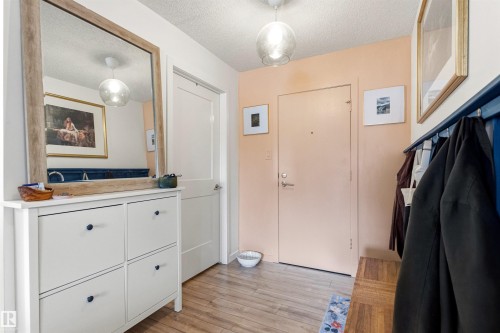 Entryway featuring wood-finish flooring, two modern ceiling lights, a white paneled interior door, and a built-in coat rack with bench seating - 217 14819 51 Avenue, Edmonton, AB - Indoor
