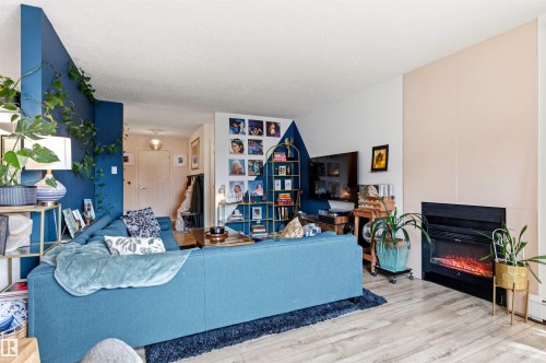 Living area featuring wood-finish flooring, a built-in fireplace with a dark surround, and a partial accent wall - 217 14819 51 Avenue, Edmonton, AB - Indoor With Fireplace