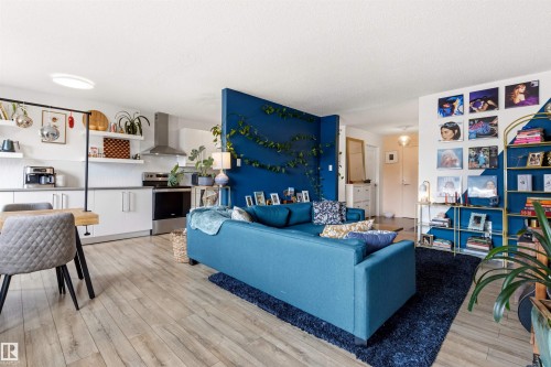 Open-concept living space featuring wood-finish flooring, a kitchen with stainless steel appliances, white cabinetry, and floating shelves - 217 14819 51 Avenue, Edmonton, AB - Indoor Photo Showing Other Room