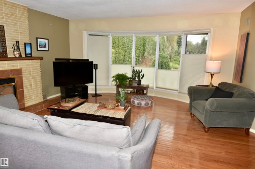 Living area featuring wood-finish flooring, a fireplace with a tiled surround and mantel, and a bay window with natural light - 13910 101A Avenue, Edmonton, AB - Indoor Photo Showing Living Room With Fireplace