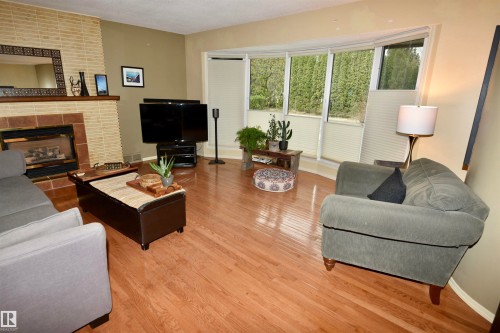 Living area featuring wood-finish flooring, a brick fireplace with a tile hearth, and a bay window with privacy shades - 13910 101A Avenue, Edmonton, AB - Indoor Photo Showing Living Room With Fireplace