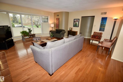 Spacious living area featuring polished wood-finish flooring, a curved architectural wall detail, and an expansive window line - 13910 101A Avenue, Edmonton, AB - Indoor Photo Showing Living Room