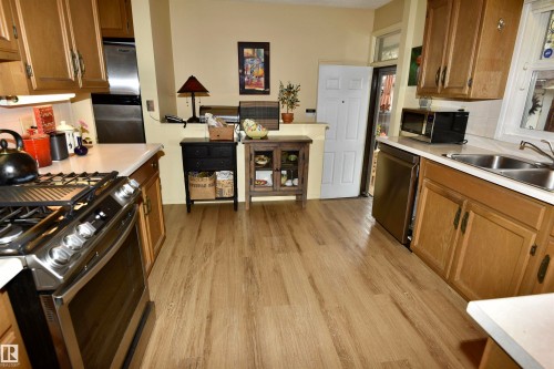 Kitchen featuring wood-finish flooring, light wood cabinetry, white countertops, and stainless steel appliances including a range and dishwasher - 13910 101A Avenue, Edmonton, AB - Indoor Photo Showing Kitchen With Double Sink