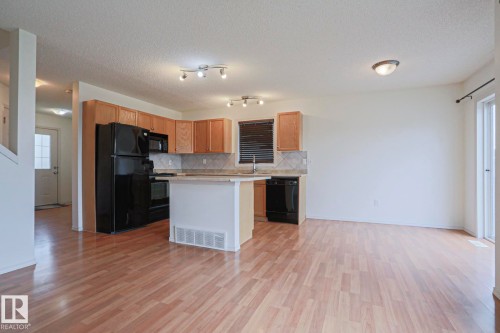 Open-concept living area featuring wood-finish flooring, a kitchen with natural wood cabinetry, black appliances, a tile backsplash, and a breakfast bar - 1627 Melrose Place Sw, Edmonton, AB - Indoor Photo Showing Kitchen