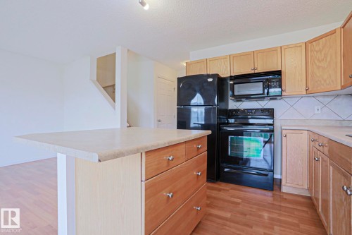 Kitchen featuring light wood cabinetry, black appliances, light-toned countertops, and a tile backsplash - 1627 Melrose Place Sw, Edmonton, AB - Indoor Photo Showing Kitchen