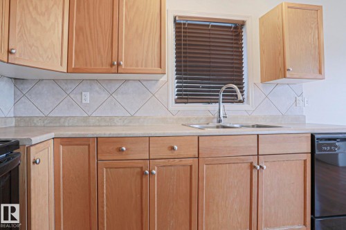 Kitchen featuring a double-basin stainless steel sink with gooseneck faucet, light wood cabinetry, and a neutral tile backsplash set in a diamond pattern - 1627 Melrose Place Sw, Edmonton, AB - Indoor Photo Showing Kitchen With Double Sink