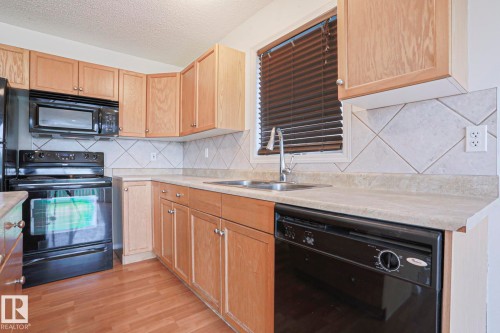 Kitchen featuring wood-finish cabinetry, black appliances, laminate countertops, and a diagonal tile backsplash - 1627 Melrose Place Sw, Edmonton, AB - Indoor Photo Showing Kitchen With Double Sink