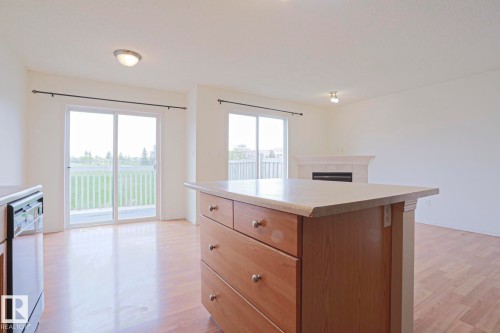 Kitchen island with a light-toned countertop and wood-finish cabinetry, wood-finish flooring, and two sets of glass sliding doors with white frames - 1627 Melrose Place Sw, Edmonton, AB - Indoor Photo Showing Kitchen