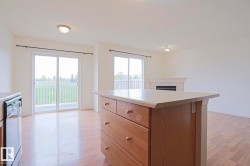 Kitchen island with a light-toned countertop and wood-finish cabinetry, wood-finish flooring, and two sets of glass sliding doors with white frames - 
