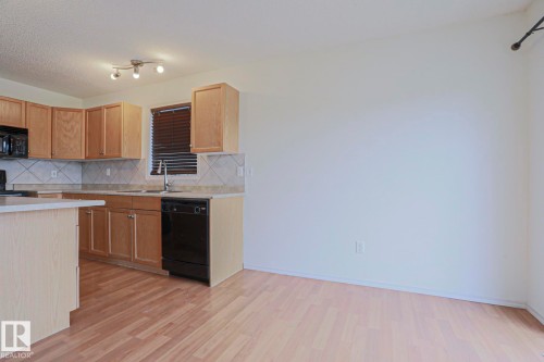 Kitchen featuring light wood cabinetry, a built-in black microwave, a black dishwasher, and a tile backsplash - 1627 Melrose Place Sw, Edmonton, AB - Indoor Photo Showing Kitchen