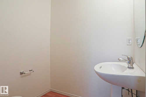 White wall finishes complement the wood-finish flooring in this space featuring a modern pedestal sink with a chrome faucet - 1627 Melrose Place Sw, Edmonton, AB - Indoor Photo Showing Bathroom