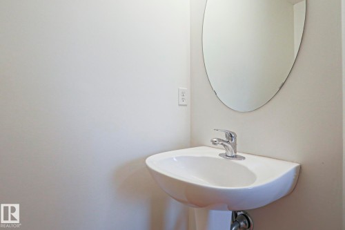 Pedestal sink with chrome faucet and an oval wall-mounted mirror - 1627 Melrose Place Sw, Edmonton, AB - Indoor Photo Showing Bathroom