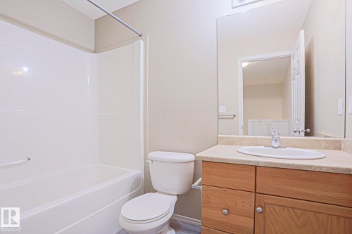 Full bathroom featuring a white tub/shower combination, a toilet, a vanity with wood-finish cabinetry, a light-toned countertop, and an integrated basin sink - 1627 Melrose Place Sw, Edmonton, AB - Indoor Photo Showing Bathroom