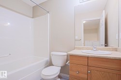Full bathroom featuring a white tub/shower combination, a toilet, a vanity with wood-finish cabinetry, a light-toned countertop, and an integrated basin sink - 