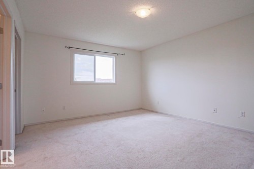 Neutral-toned carpeting extends throughout this room, featuring light-colored walls and a single window with a white frame - 1627 Melrose Place Sw, Edmonton, AB - Indoor Photo Showing Other Room