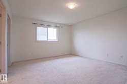 Neutral-toned carpeting extends throughout this room, featuring light-colored walls and a single window with a white frame - 