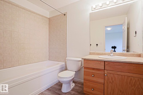 Bathroom featuring a white bathtub with beige tiled surround, a toilet, and a wood-finish vanity with an integrated sink and light-colored countertop - 1627 Melrose Place Sw, Edmonton, AB - Indoor Photo Showing Bathroom