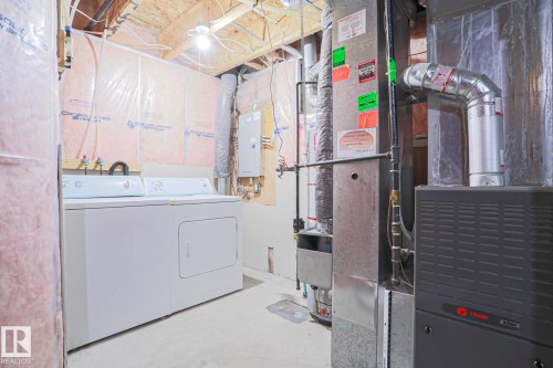 Utility area featuring a furnace system, water heater, water lines, and exposed insulation - 1627 Melrose Place Sw, Edmonton, AB - Indoor Photo Showing Laundry Room
