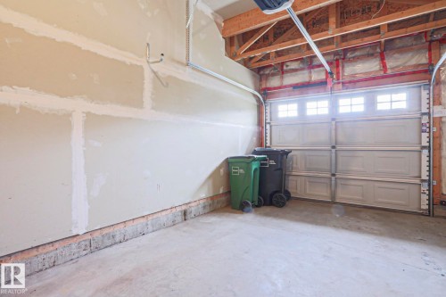 Attached garage featuring a concrete floor, light-colored walls, and an overhead garage door with upper window inserts - 1627 Melrose Place Sw, Edmonton, AB - Indoor Photo Showing Garage