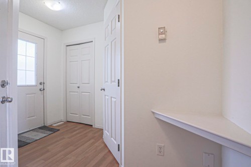 Entryway featuring wood-finish flooring, a contemporary ceiling light fixture, a built-in wall shelf, a modern thermostat, and multiple interior doors - 1627 Melrose Place Sw, Edmonton, AB - Indoor Photo Showing Other Room