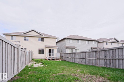 Rear exterior featuring light-toned siding, a rear wood deck, and a grass lawn - 1627 Melrose Place Sw, Edmonton, AB - Outdoor With Exterior