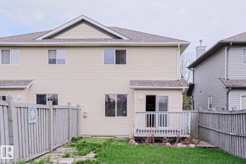 Rear exterior featuring beige horizontal siding, white-framed windows, and a multi-level roofline - 1627 Melrose Place Sw, Edmonton, AB - Outdoor With Deck Patio Veranda With Exterior