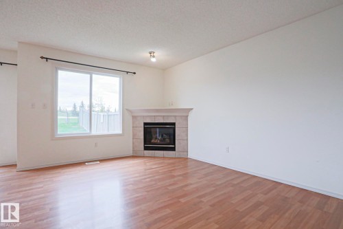 Bright interior space featuring wood-finish flooring and white walls - 1627 Melrose Place Sw, Edmonton, AB - Indoor Photo Showing Living Room With Fireplace