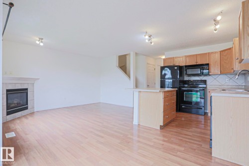 Open-concept living space featuring wood-finish flooring, a tiled fireplace, and track lighting - 1627 Melrose Place Sw, Edmonton, AB - Indoor Photo Showing Kitchen With Fireplace