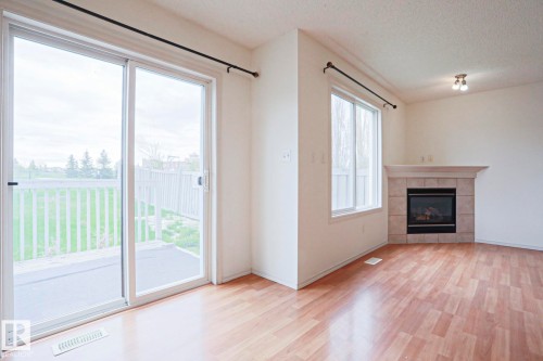Living space featuring wood-finish flooring, a white trim window, and a tile-surround fireplace with a mantel - 1627 Melrose Place Sw, Edmonton, AB - Indoor Photo Showing Living Room With Fireplace